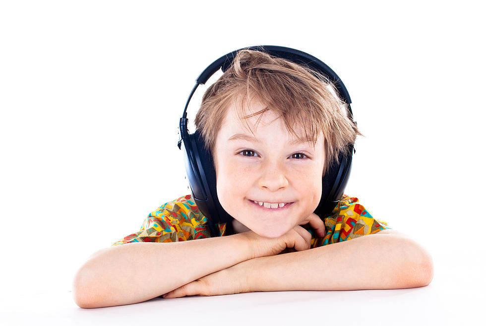 Junge mit Kopfhörern stützt sich auf seine Arme und lächelt in die Kamera.