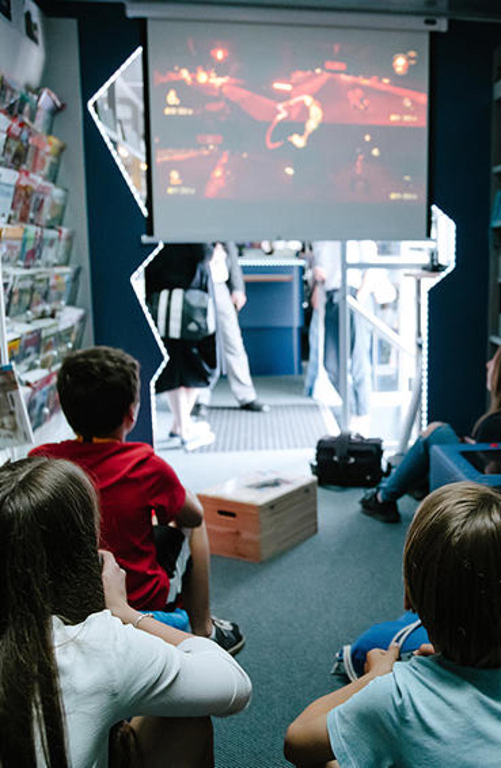 Kinder genießen eine Filmvorführung in einem Bücherbus, der mit Beamer und Leinwand ausgestattet ist.