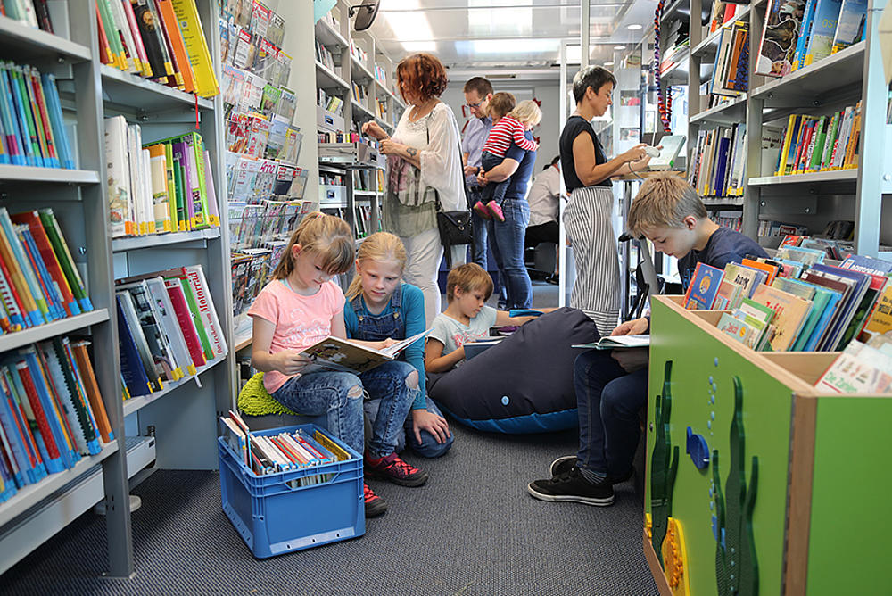 Erwachsene und Kinder suchen in einem Bücherbus nach passendem Lesematerial.