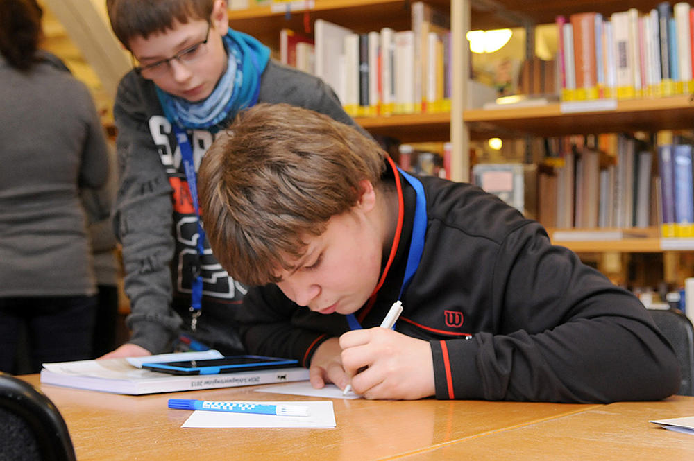 Ein Junge sitzt an einem Schreibtisch in einer Bücherei, die eine QR-Code-Rallye mit James Bound veranstaltet.